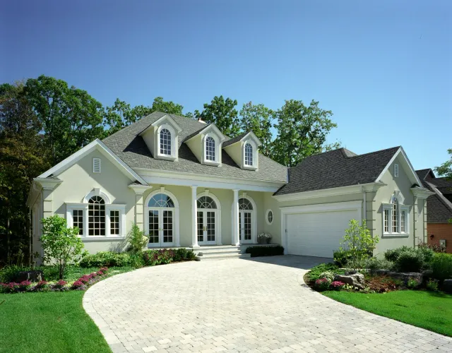 Elegant beige house with white trim, arched windows, and a winding stone driveway on a sunny day.
