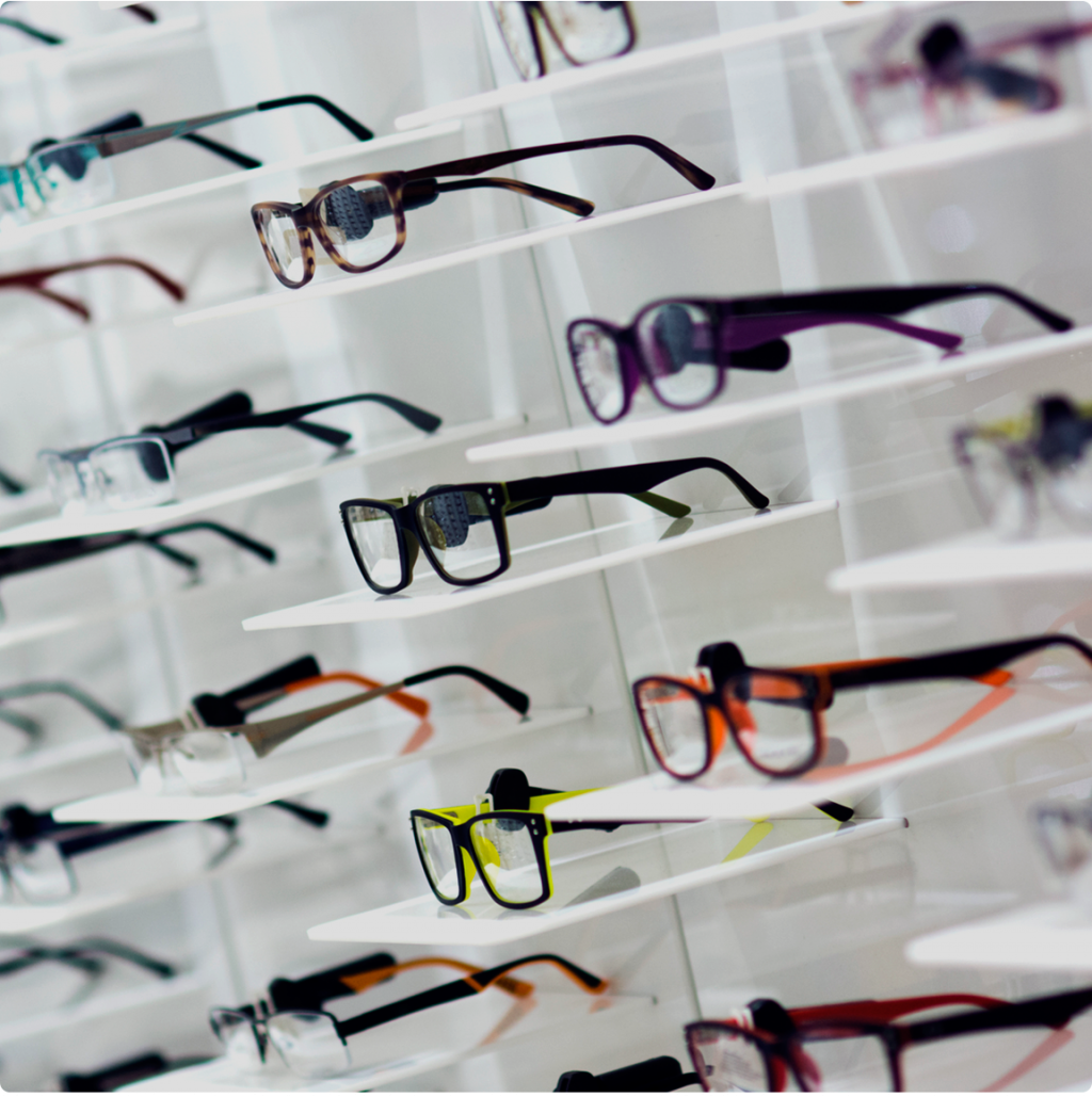 En una tienda, se exhiben varios pares de gafas con monturas de diferentes colores y estilos en estantes blancos.