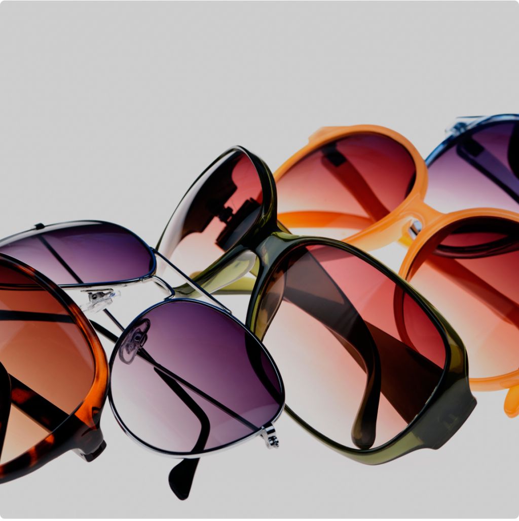 Una colección de gafas de sol coloridas con lentes de tinte degradado, dispuestas sobre un fondo gris claro.