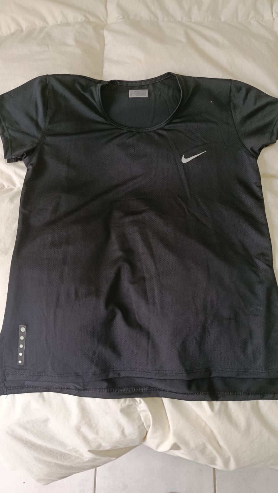 Camiseta negra de Nike extendida sobre una colcha blanca, con un pequeño logotipo blanco de Swoosh.