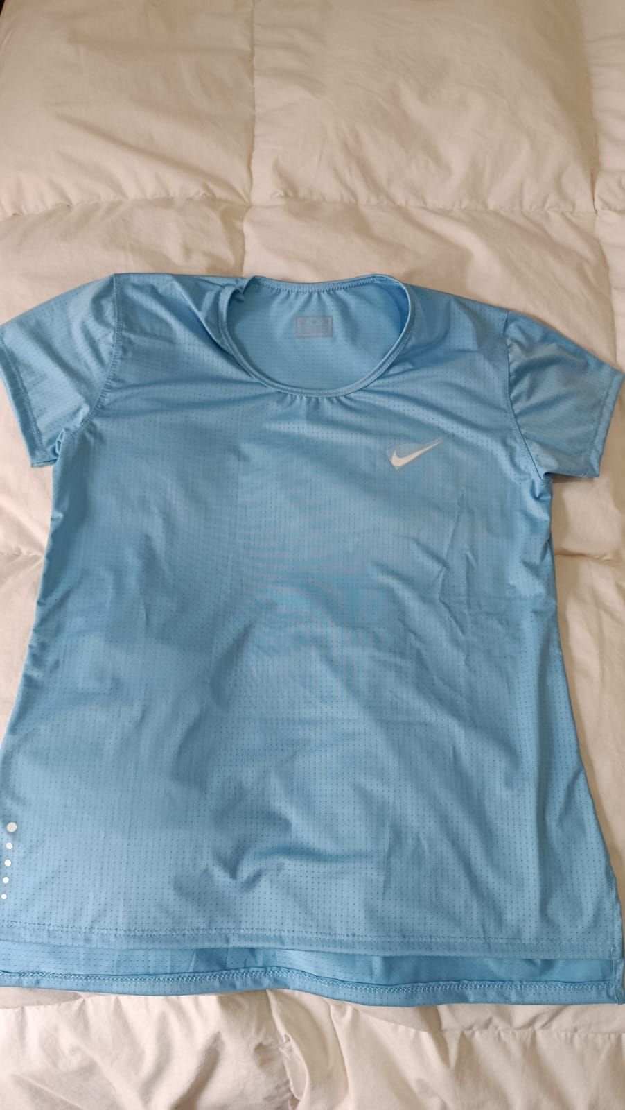 Camiseta negra de Nike extendida sobre una colcha blanca, con un pequeño logotipo blanco de Swoosh.