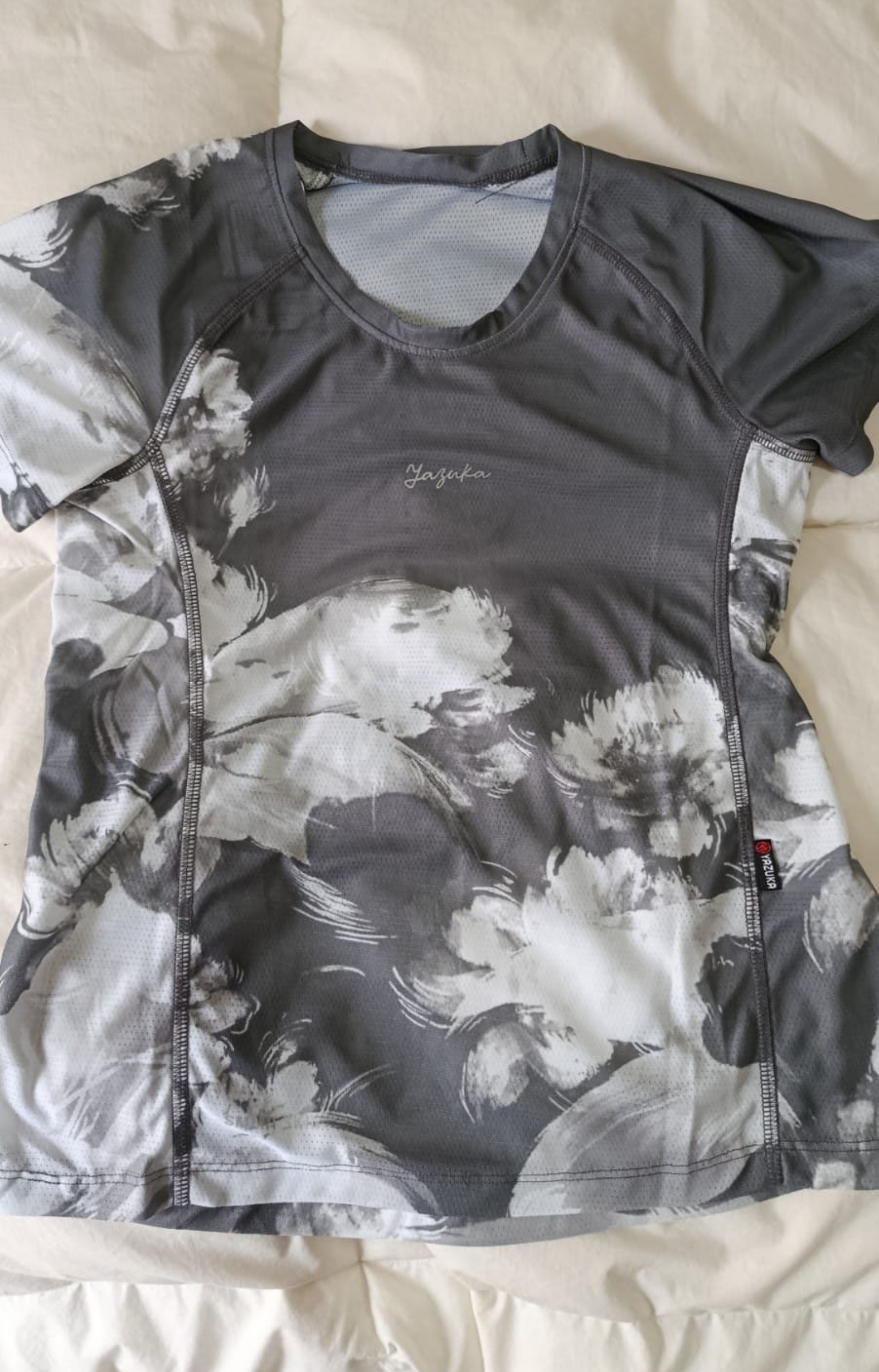 Camiseta de manga corta con cuello en V, teñida con efecto tie-dye en gris y blanco, extendida sobre una cama