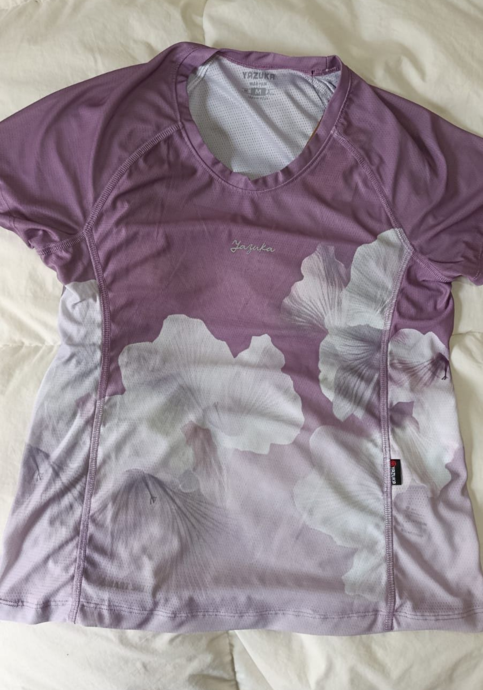 Camiseta de manga corta con cuello en V, teñida con efecto tie-dye en gris y blanco, extendida sobre una cama