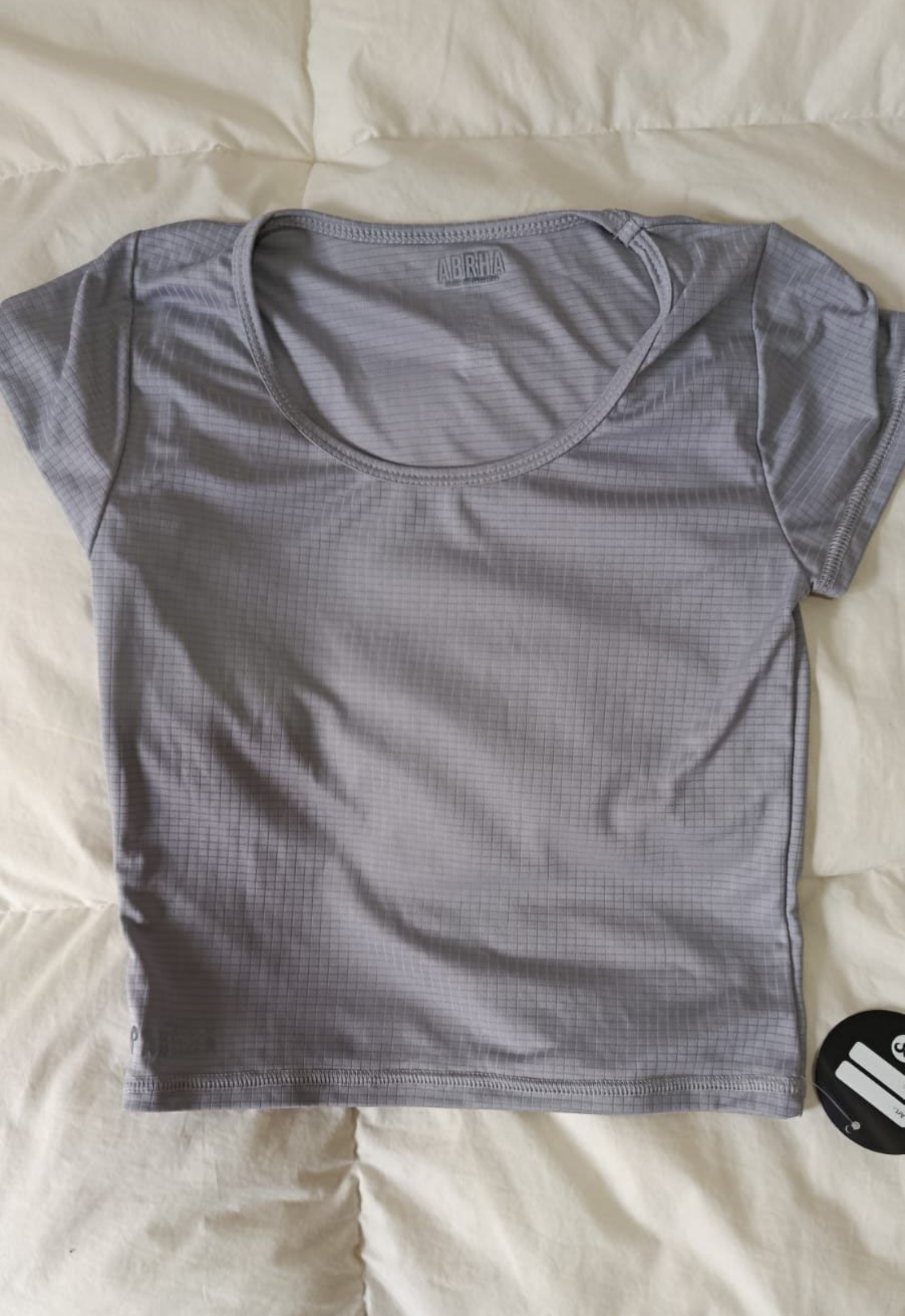 Camiseta gris de manga corta extendida sobre una cama o una superficie de color claro.