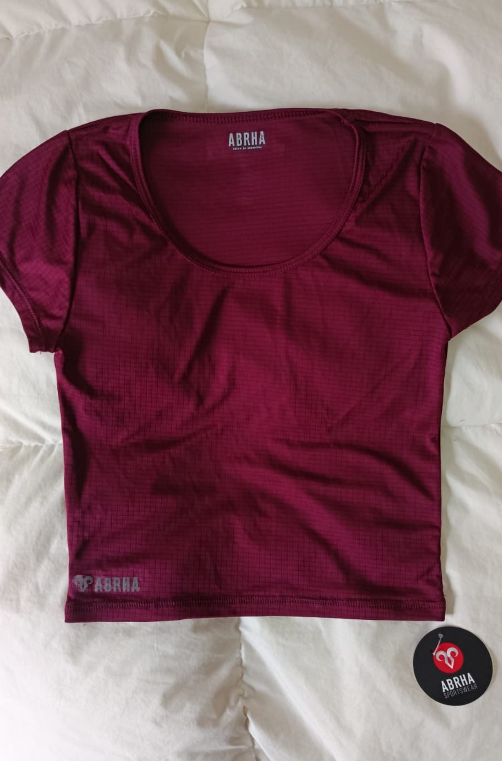 Camiseta gris de manga corta extendida sobre una cama o una superficie de color claro.