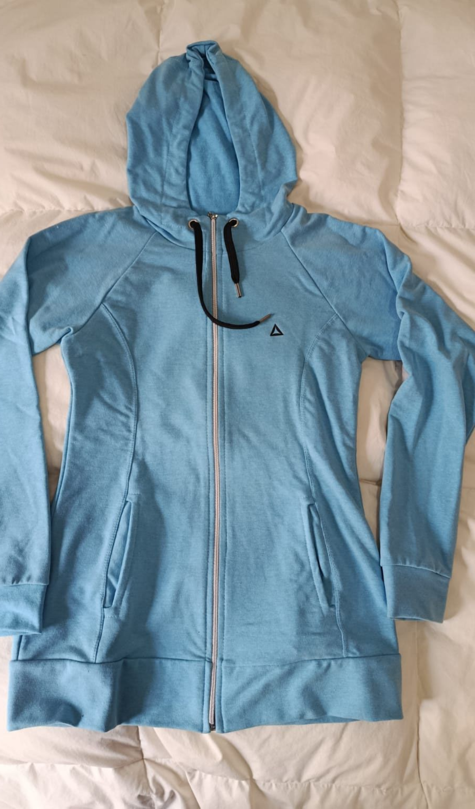 Chaqueta azul claro con capucha y cremallera, extendida sobre una superficie blanca
