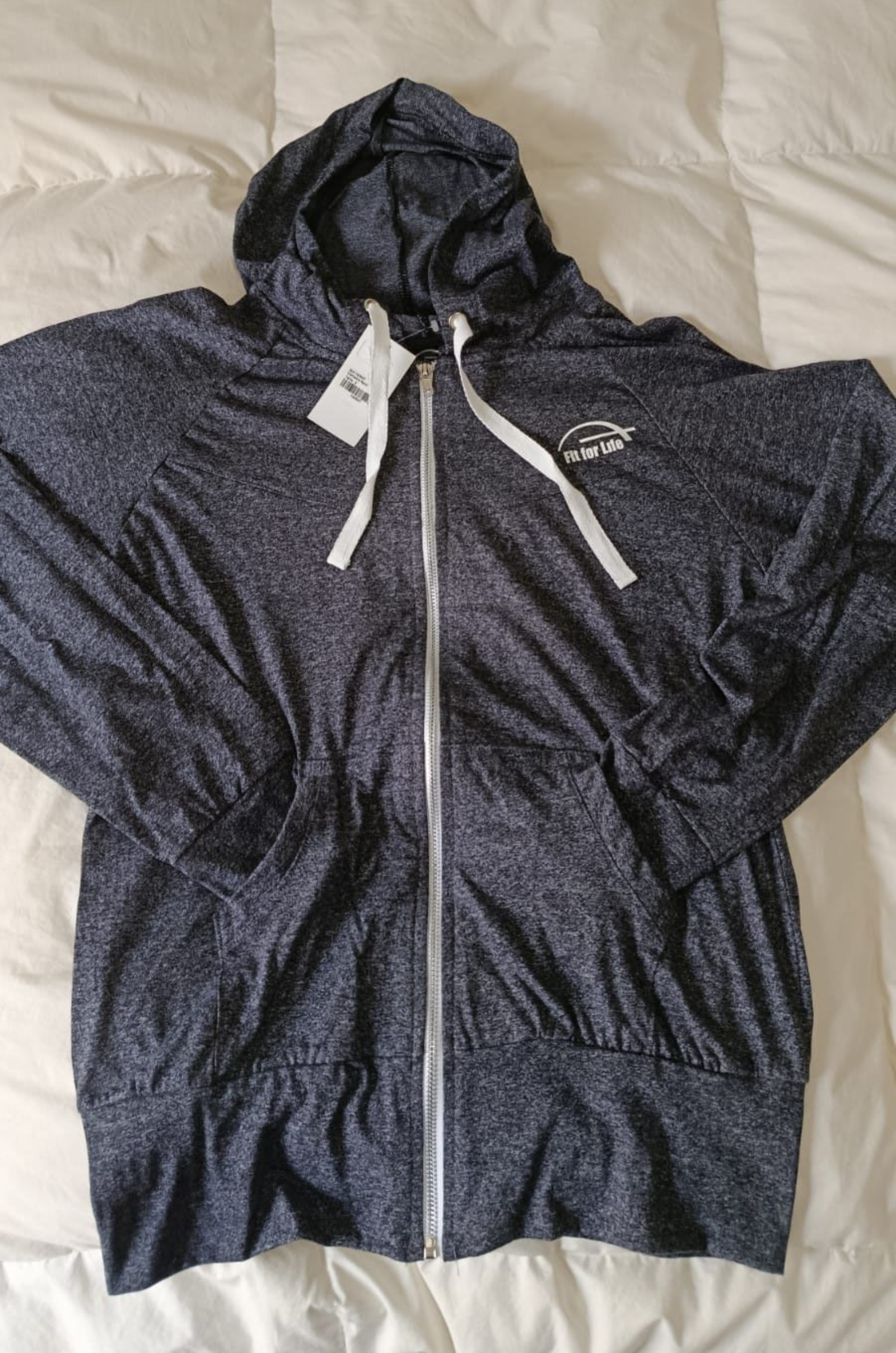 Sudadera gris oscuro con capucha, cremallera y cordones blancos, extendida sobre una cama.