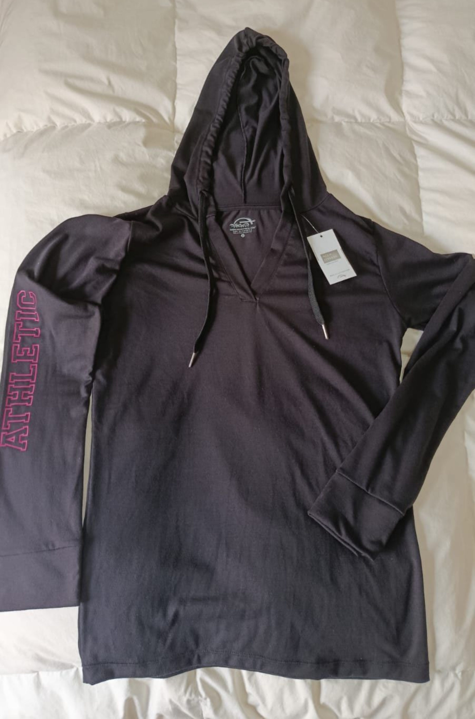 Camisa de manga larga con capucha, de color morado oscuro y con un estampado rosa en la manga, extendida sobre una cama.