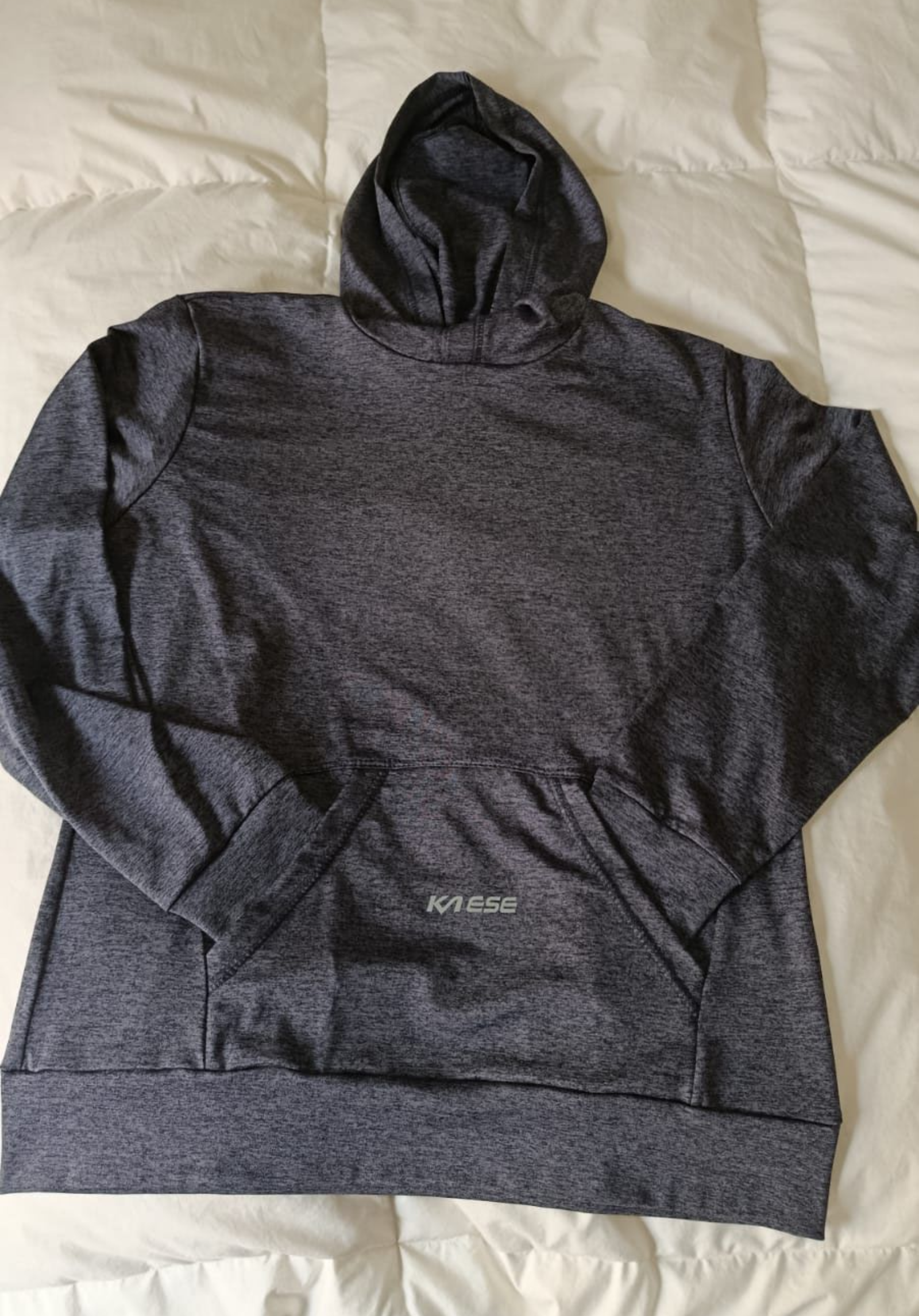Sudadera con capucha de color gris oscuro extendida sobre una cama, con las mangas abiertas