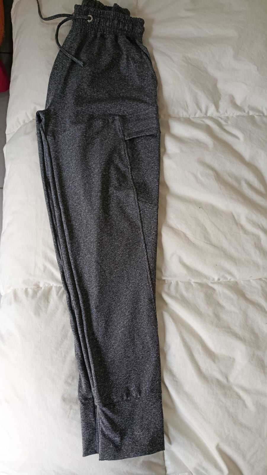 Pantalones grises estampados extendidos sobre una colcha blanca.