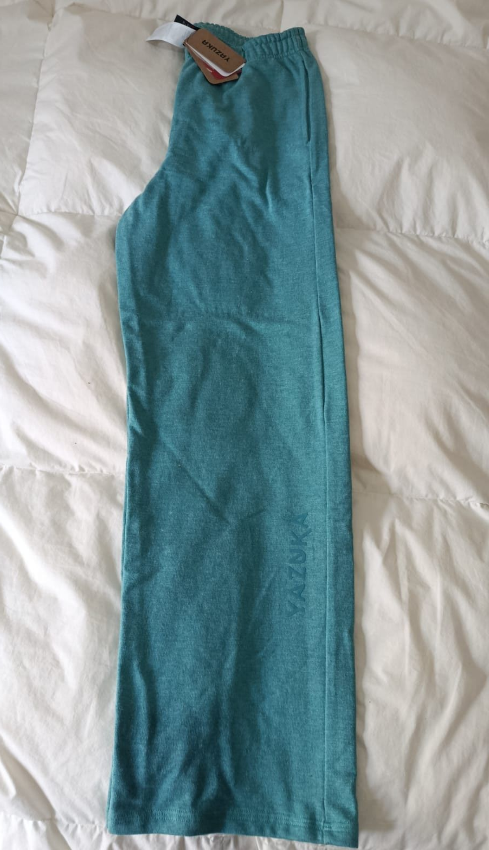 Vestido largo sin mangas de color verde azulado, extendido sobre una colcha blanca.