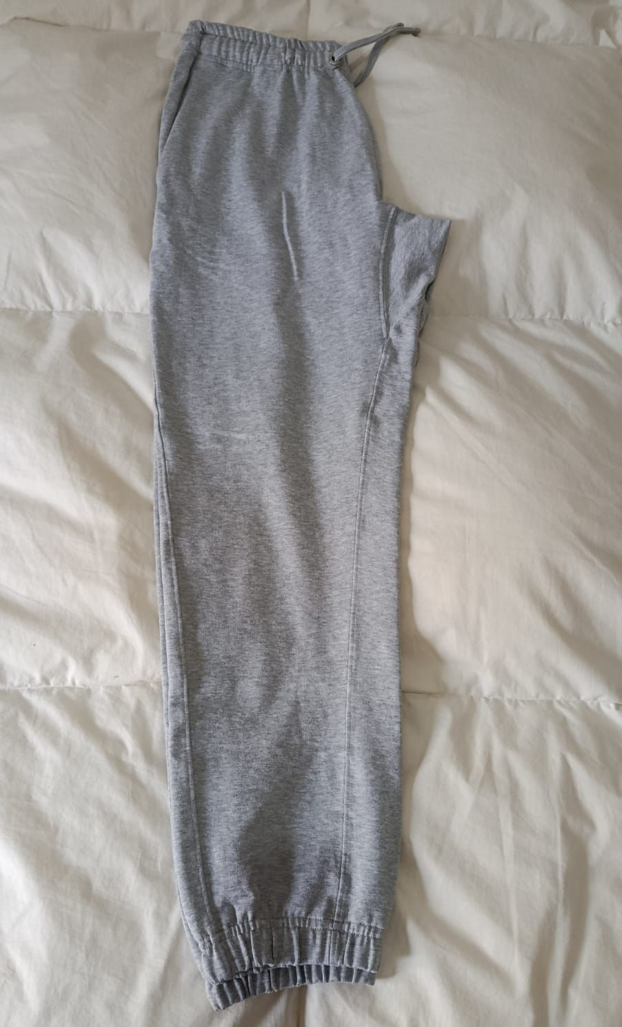 Pantalón deportivo de punto gris, extendido sobre una cama blanca.