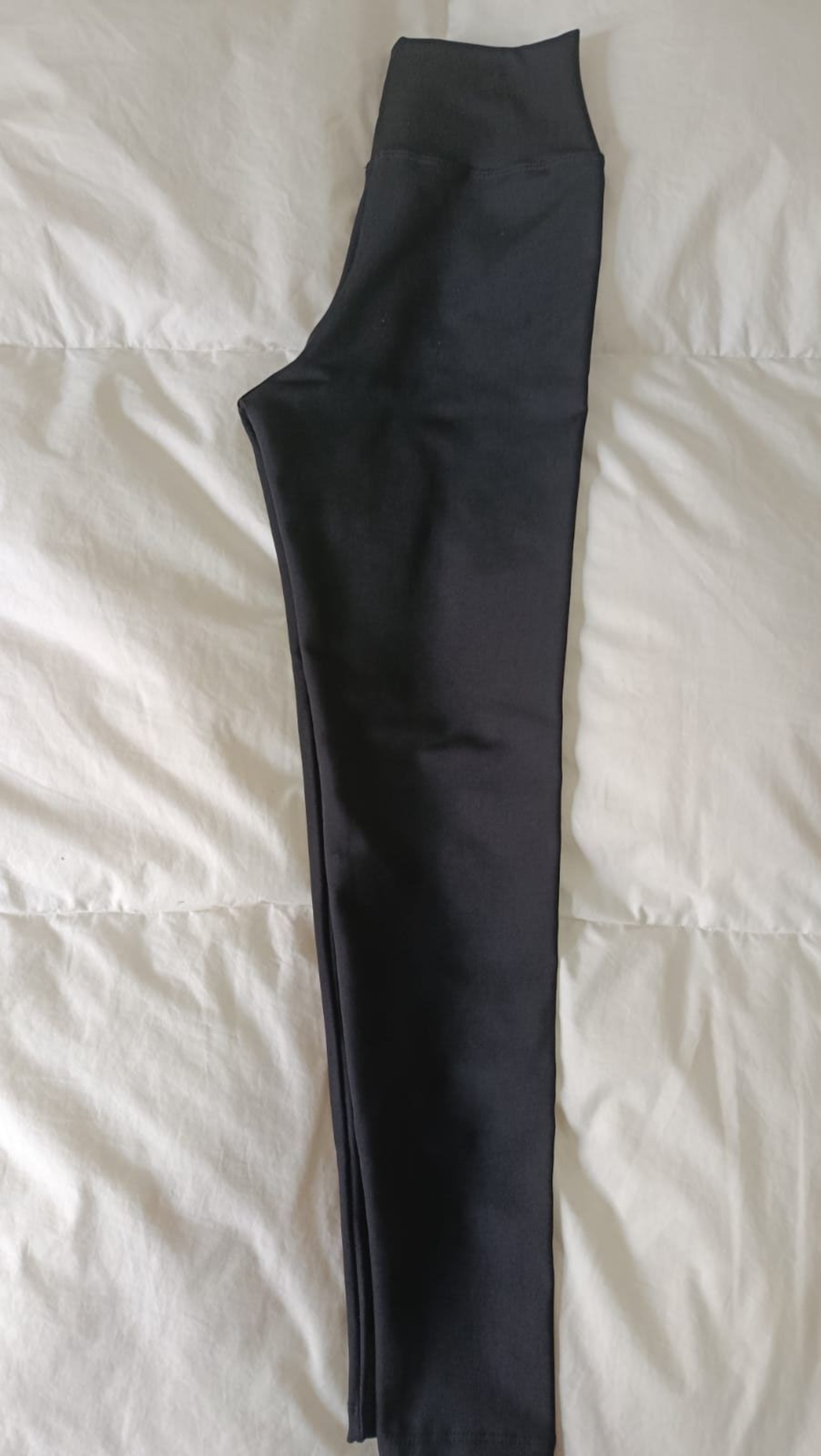 Pantalones negros extendidos sobre una colcha blanca.