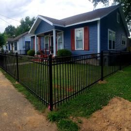 Blue house with white porch columns and a black metal fence along the front yard