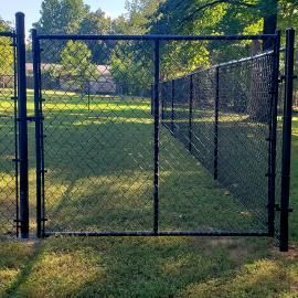Black chain-link fence gate in a grassy yard with trees in the background