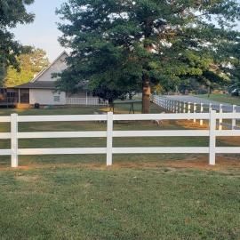 White fenced yard with a large tree and a house in the background at dusk