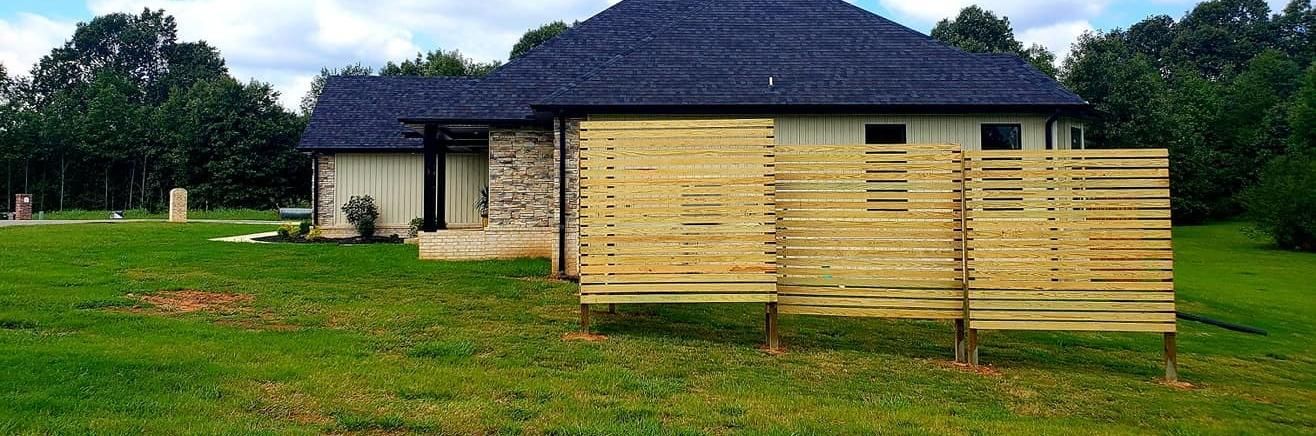 Stone house with dark roof and a wooden fence in a grassy yard under overcast skies