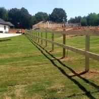 Wooden fence posts lining a green field under a sunny sky