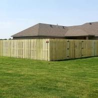 Wooden privacy fence around a grassy backyard beside a tan-roofed house