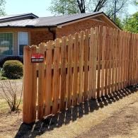 Wooden slatted fence with a red warning sign beside a brick house in a yard