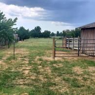 Rural yard with patchy grass, a fenced pen, and a small shed under cloudy skies