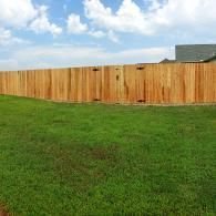 Grassy yard with a long wooden fence under a partly cloudy sky