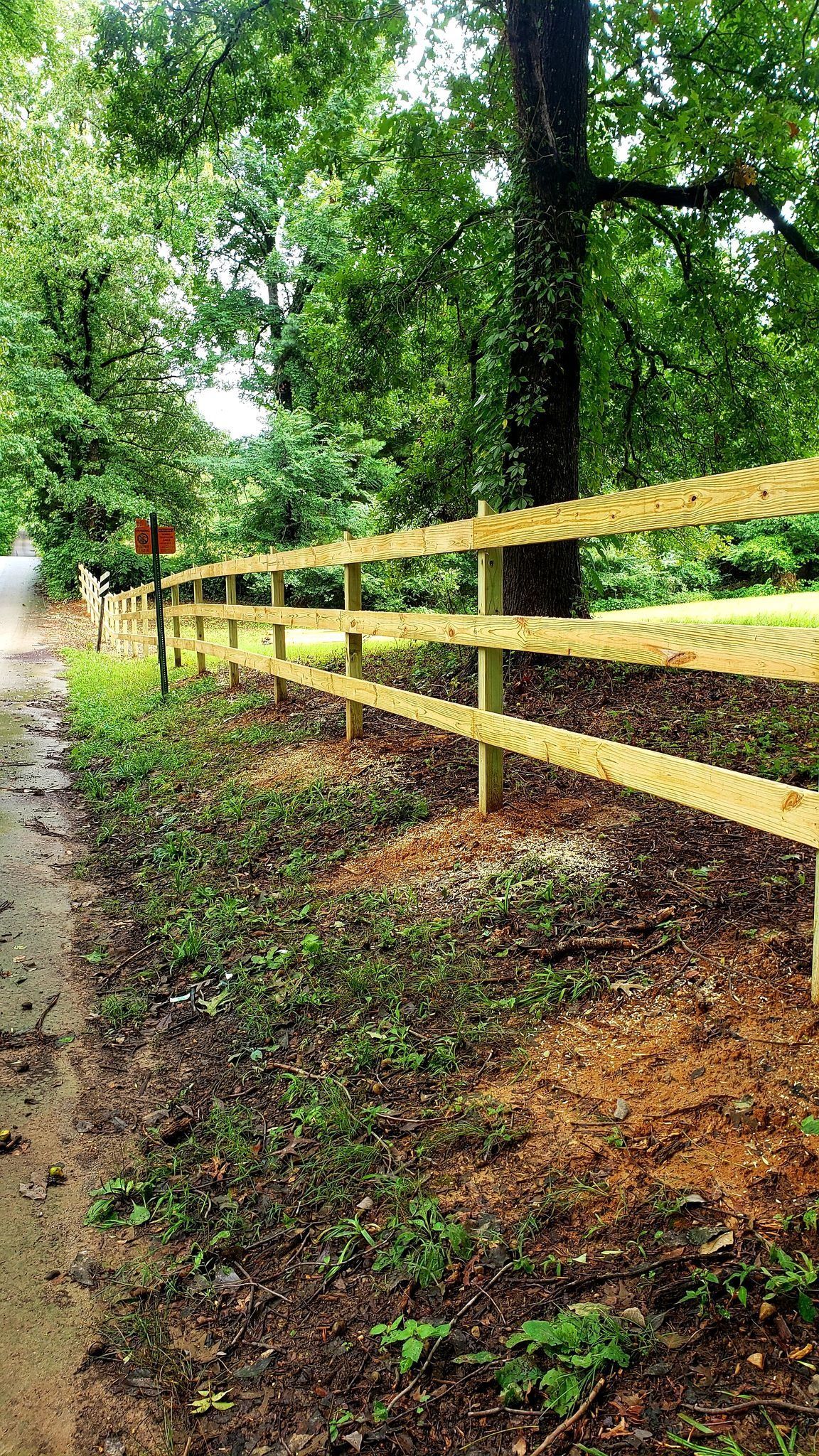 Yellow wooden fence along a muddy wooded path in a rainy green park