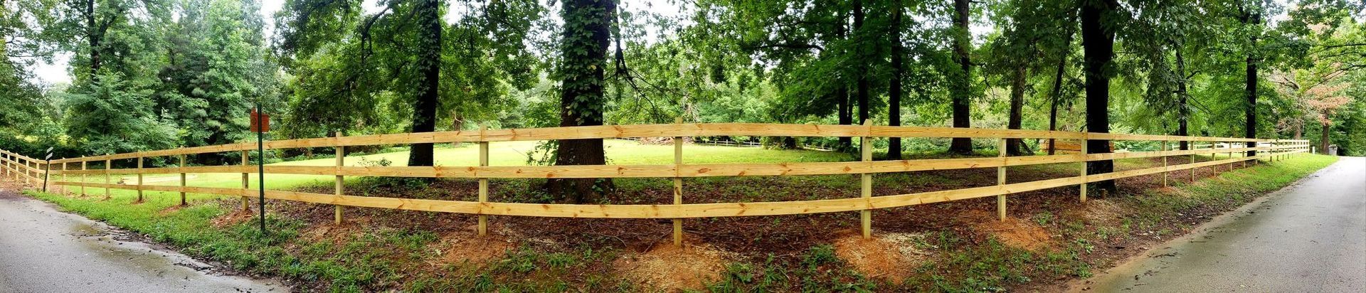 Yellow wooden fence around a grassy wooded path beside a road