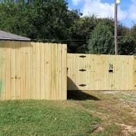 Wooden privacy fence with black patches beside a grassy yard under a blue sky