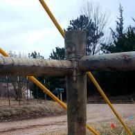 Wooden fence rails with yellow diagonal supports beside a dirt road and trees