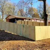 Wooden privacy fence surrounding a house in a wooded yard on a sunny day
