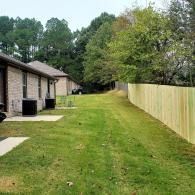 Backyard beside townhouses with green lawn, trees, and a long wooden fence