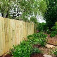 Wooden fence beside a lush garden path with stepping stones and overhanging green trees