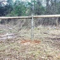 Wooden fence post with horizontal rail in a grassy, wooded area