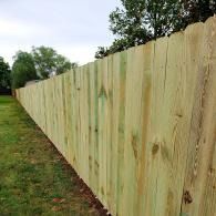 Long wooden privacy fence beside a grassy yard with trees in the background