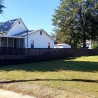 Suburban houses beside a fenced backyard with a grassy lawn and a large tree