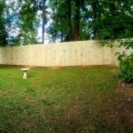 Grassy backyard with a tall wooden fence and trees, plus a small birdbath on the left