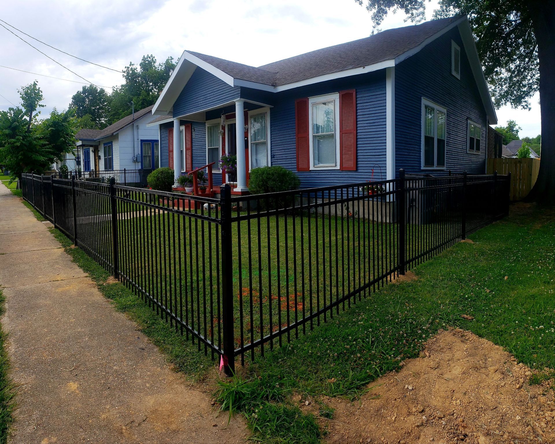 Blue house with red shutters behind a black metal fence along a gravel path