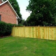 Backyard with green lawn, wooden fence, brick house, and large trees