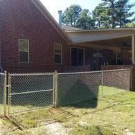 Brick house with a chain-link fence and grassy yard in front, under trees.
