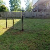 Backyard with a chain-link fence, green grass, and a house deck in the background