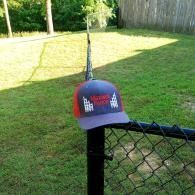 Gray baseball cap on a black fence post beside a chain-link fence in a sunny backyard
