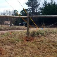 Wooden fence by a dirt road in a grassy rural area, with trees and power lines in the background