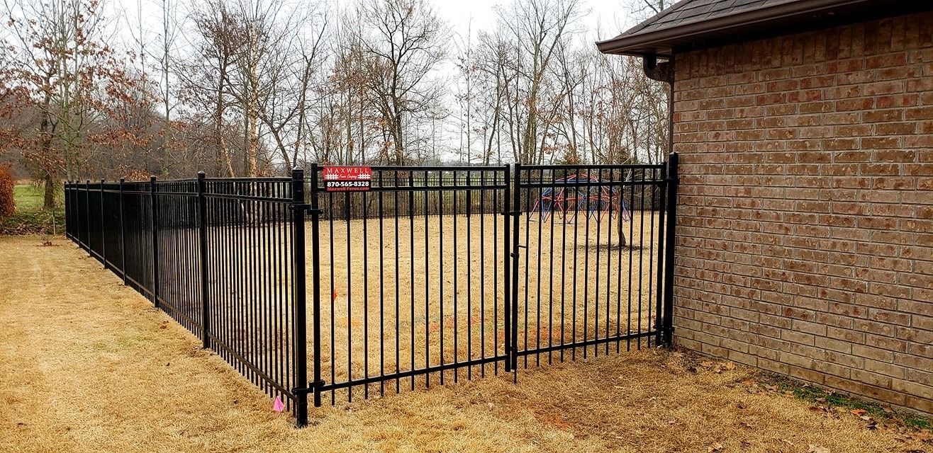 Black metal fence beside a brick building enclosing a leaf-covered yard