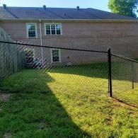 Backyard with black chain-link fence, green grass, and a brick house in the background