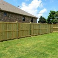 Backyard with wooden privacy fence beside a brick house and green lawn