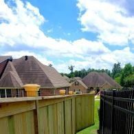 Suburban rooftops behind a wooden fence under a bright blue sky with scattered clouds