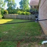 Backyard with chain-link fence, grassy lawn, wooden privacy fence, and house in the background
