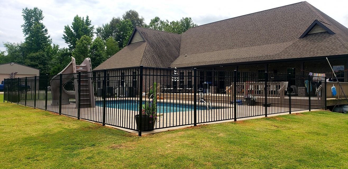 Outdoor swimming pool with black fence beside a tan building and grassy lawn