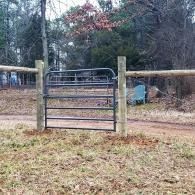 Metal farm gate between wooden posts on a dirt path in a wooded area